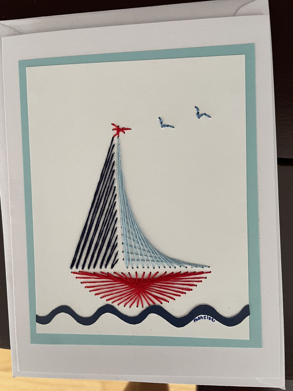 Voilier brodé sur papier, voiles bleu marine et bleu clair, coque rouge